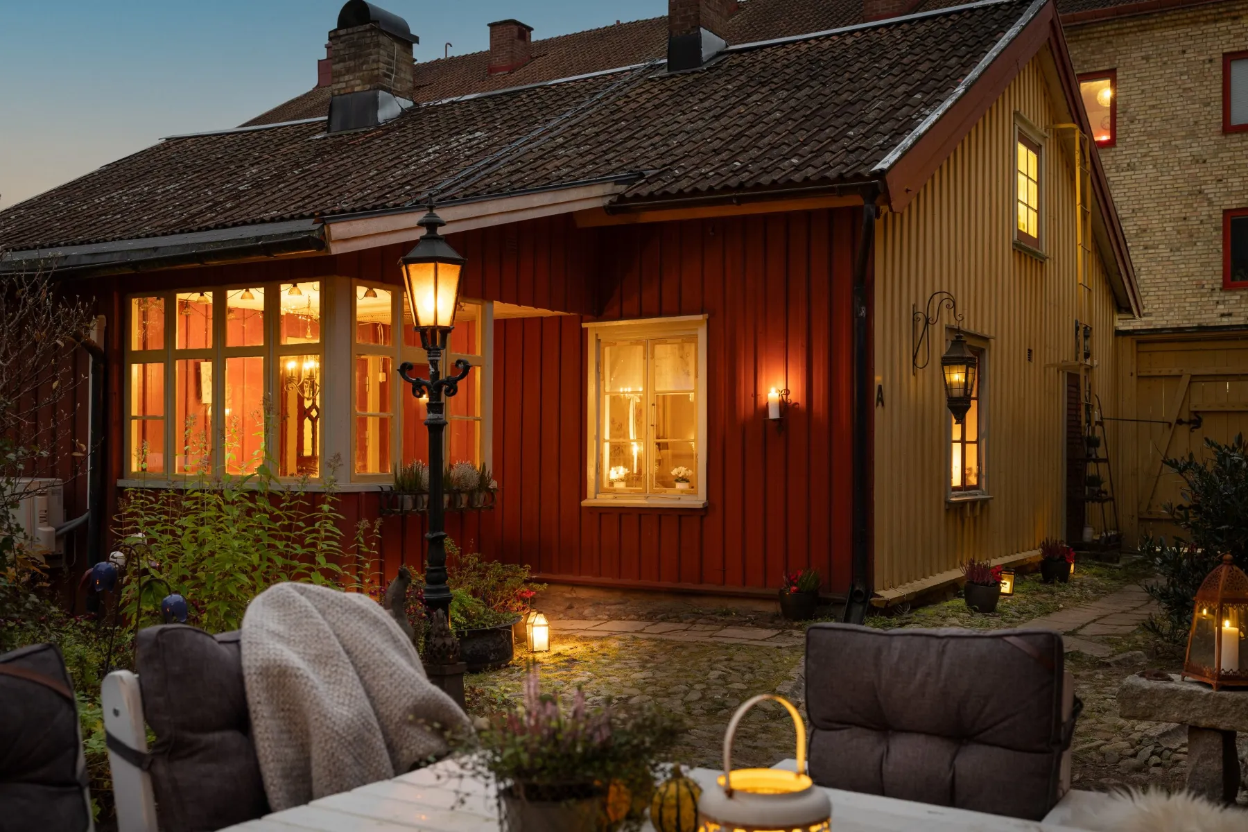 Skymningsfoto 11 Rött trähus med tända fönster, lykta och fällar på uteplatsen en kväll