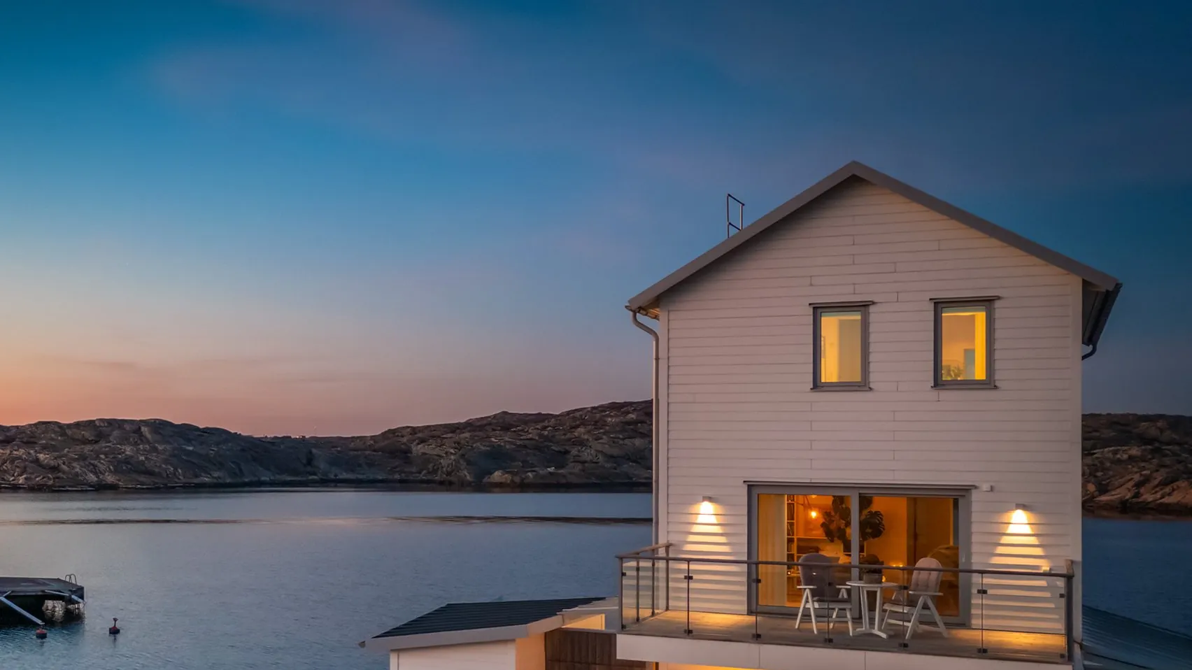 Skymningsfoto 1 Vitt hus vid havet i skymningen, med tända fönster och upplyst balkong